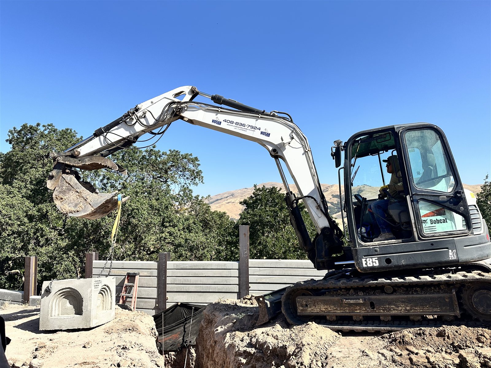 A Vidsan Builders excavator on an active job site, branded with the company logo and phone number